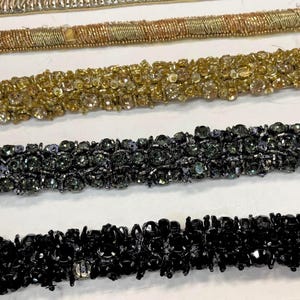 Op de afbeelding: Close-up van verschillende decoratieve sierlijsten in verschillende kleuren. De sierlijsten bevatten gouden, zwarte en zilveren kralenontwerpen. De sierlijsten zijn horizontaal gerangschikt en tonen hun texturen en details. Ideaal voor het verfraaien van kleding of ambachten.