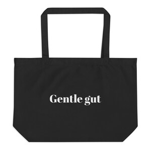 May include: Black tote bag with the text "Gentle gut" in white. The bag has a rectangular shape with a large open compartment and two long handles for carrying over the shoulder.