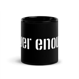 May include: A white ceramic mug with a black handle and the text "But First, Coffee" in a bold, black font. The mug is set against a blurred background, suggesting a cozy setting.