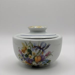 Peut inclure: Un sucrier en céramique blanche avec un couvercle, orné d'un motif floral de jonquilles, d'iris et d'autres fleurs colorées. Le bol a une bordure bleue et un couvercle assorti avec un motif floral jaune.