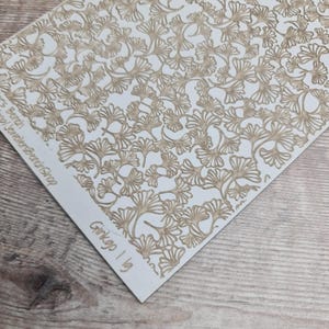 May include: A white paper with a repeating pattern of tan ginkgo leaves. The leaves are detailed with visible veins and are arranged in a dense, overlapping design. The text "Ginkgo I lg" is printed in the bottom corner.