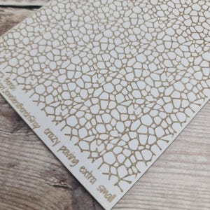 May include: A white card with a repeating pattern of irregular, interconnected shapes in a light brown color. The text "crazy paving extra small" is printed in a matching brown color. The card is slightly angled, showing a corner.