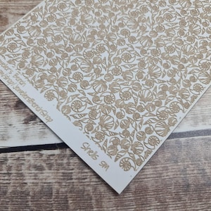 May include: A white paper featuring a repeating pattern of tan seashells and floral designs. The text "Jeweler's Bench Shop" and "Shells SM" are printed on the paper.