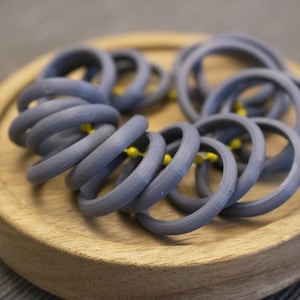 May include: A close-up of a pile of gray silicone rings on a wooden surface. The rings are stacked on top of each other and are all the same size.