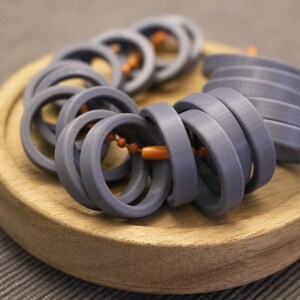 May include: A close-up of a stack of gray plastic rings, some of which are interlocked. The rings are arranged in a circular pattern on a wooden surface.