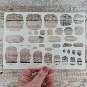 Puede incluir: Una plantilla de plástico blanco con múltiples formas ovaladas de diferentes tamaños. La plantilla está diseñada para manualidades y la creación de diseños únicos.