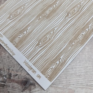 May include: A sheet with a woodgrain pattern in shades of brown and white. The design features parallel lines and curved details to mimic the texture of wood. The text "Woodgrain SM" is visible on the bottom right corner.
