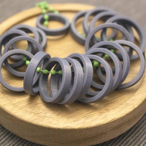Könnte beinhalten: Eine Ansammlung grauer, kreisförmiger Ringe, die mit einer grünen Perlenkette aufgereiht sind. Die Ringe sind in einer gebogenen Form angeordnet und liegen auf einem Holztablett. Die Ringe scheinen aus einem festen Material zu bestehen.