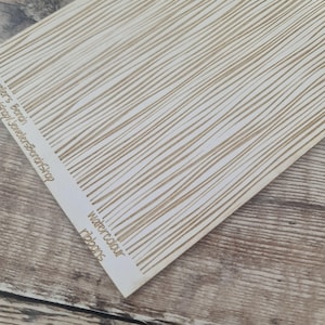 May include: A sheet of paper with a pattern of thin, parallel, light brown lines on a white background. The words "watercolour ribbons" are printed on the bottom right corner. The text "JewellersBenchShop" is printed on the left side.