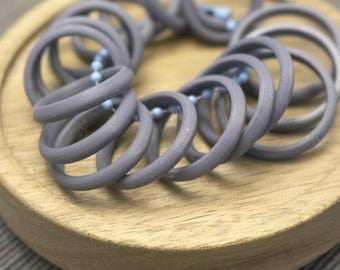 May include: A collection of matte grey circular rings linked together by a light blue ball chain. The rings are arranged in a cluster, showcasing a smooth, uniform finish on each individual circular component, creating a cohesive set of items.