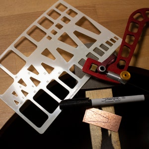 May include: A white plastic template with various shapes and sizes, a red metal tool with a knob, a black Sharpie marker, and a piece of copper with a cut-out shape.