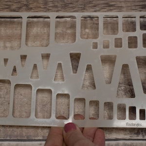 Puede incluir: Una plantilla de plástico transparente con varias formas, incluyendo triángulos y rectángulos. La plantilla está etiquetada como "Rectangles" y tiene medidas en pulgadas.