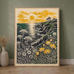 May include: A framed rectangular wall art print featuring a coastal landscape at sunset. The scene depicts a dark green ocean with rocky cliffs, a yellow sun, and clouds. The foreground shows detailed white and yellow wildflowers and foliage.