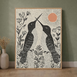 Op de afbeelding: Een ingelijste kunstdruk met een zwart-witte inktillustratie van twee kolibries die tegenover elkaar staan met hun snavels tegen elkaar. Een cirkelvormige perzikkleurige zon met stralen bevindt zich boven de vogels tussen het bloemrijke gebladerte.