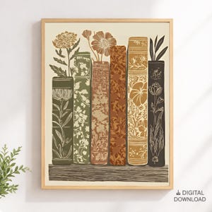 May include: A framed wall art print featuring a row of six vertical books standing on a shelf. The book spines are decorated with intricate botanical illustrations of flowers and leaves in shades of olive green, brown, and cream.