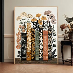 May include: A rectangular wall art print featuring a row of six vertical books with varied spine designs in black, orange, green, and white. Botanical illustrations of wildflowers, including orange and white blossoms, emerge from the top of the books.