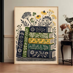 May include: A framed vertical art print featuring a stack of five books and one standing book, all decorated with botanical illustrations of flowers and leaves in shades of navy blue, forest green, and yellow against a cream background.