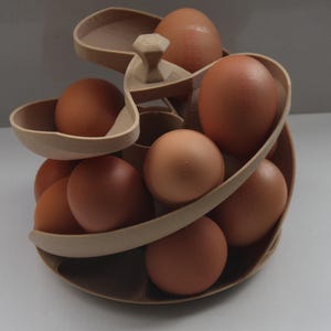 Peut inclure: Un présentoir à œufs en bois de couleur claire, en forme de spirale, rempli d'œufs bruns. Le présentoir comporte plusieurs niveaux, chacun conçu pour accueillir les œufs. Les œufs varient en teinte, du beige clair au brun foncé.