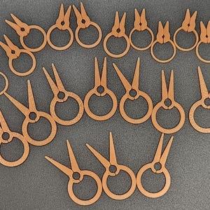 May include: A collection of small, wooden scissors with circular handles and pointed blades. The scissors are arranged on a dark gray surface. The wood has a light brown color.