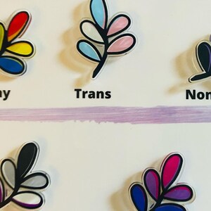 May include: Five different colored leaf designs with black outlines. The leaves are labeled "Gay", "Trans", "Non Binary", "Asexual", and "Bisexual".