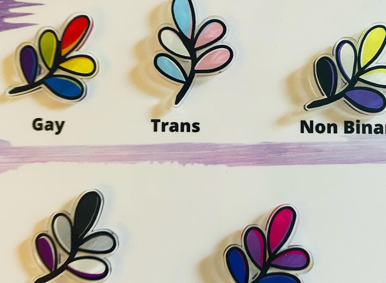 May include: Five different colored leaf designs with black outlines. The leaves are labeled "Gay", "Trans", "Non Binary", "Asexual", and "Bisexual".