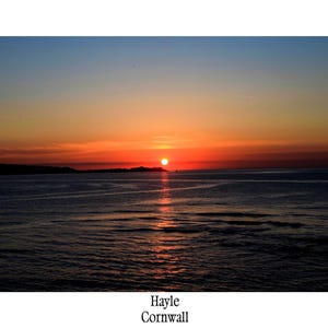 May include: A photograph of a sunset over the sea. The sky gradients from blue to orange and red, with the sun near the horizon. The water reflects the sky's colours. Text at the bottom reads "Hayle Cornwall."