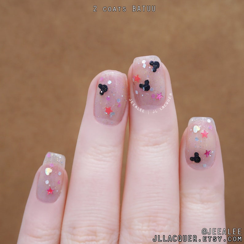 May include: Close-up of a hand with nude nail polish and glitter, featuring Mickey Mouse and star-shaped nail art. The text "2 coats Batuu" and "@jeealee jllacquer.etsy.com" are visible.