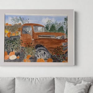 May include: Watercolor painting of a vintage orange truck in a pumpkin patch. The truck is surrounded by pumpkins and greenery, with a blue sky in the background. The artwork is framed in a white border.