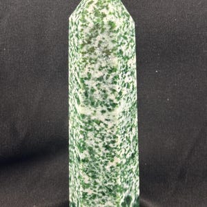 May include: A polished stone tower with a hexagonal base and a pointed top. The mineral features a mottled pattern of deep forest green and bright white crystalline inclusions distributed throughout the entire surface of the vertical structure.