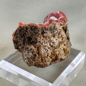 Puede incluir: Un esp&eacute;cimen mineral natural y rugoso que presenta una mezcla de texturas y colores. El exterior es marr&oacute;n y beige moteado, con una apariencia porosa. El interior revela una vibrante formaci&oacute;n de cristales rosas.