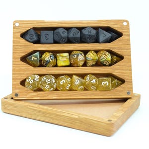 Könnte beinhalten: Geöffnete Würfelbox aus Holz mit drei Fächern. Oben befinden sich schwarze Würfel, in der Mitte gelbe und braune Würfel und unten transparente Würfel mit goldenem Glitzer. Die Box ist aus hellem Holz gefertigt.