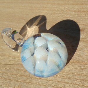 May include: A glass pendant with a blue and white swirl design. The pendant is round and has a clear glass loop for hanging.