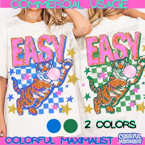 May include: Off-white t-shirts with a colorful graphic design. The design features the word "EASY" in pink and orange glitter, a tiger blowing a bubble, and stars. The text "2 COLORS" is also visible.
