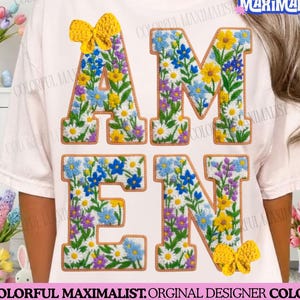 May include: A white t-shirt featuring the word "AMEN" in embroidered letters filled with colourful flowers. The letters are outlined in brown. The shirt also has two yellow bows. The text "COLORFUL MAXIMALIST" is visible.