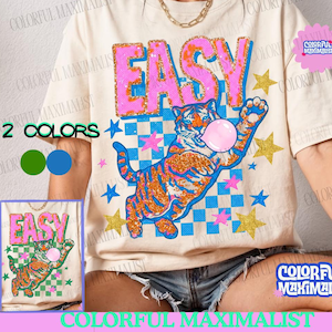 Op de afbeelding: Crèmekleurig T-shirt met het woord "EASY" in roze en oranje glitterletters. Een tijger die een kauwgomballenblaas blaast, staat onder de tekst. Het ontwerp bevat gouden sterren en blauwe en roze accenten. De tekst "COMMERCIAL USAGE" staat bovenaan.
