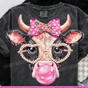 May include: A black t-shirt features a cow graphic with heart-shaped glasses, a pink polka dot bow, and a bubblegum bubble. The cow's face has floral patterns. The text "COLORFUL MAXIMALIST. ORGINAL DESIGNER" is at the bottom.