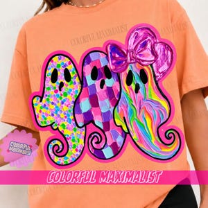 May include: An orange t-shirt featuring a graphic of three ghosts with black eyes and mouths. The first ghost has a multicolored polka dot pattern, the second has a purple and blue checkered pattern, and the third has a pink bow and swirl design.