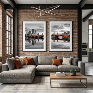 Peut inclure: Un salon moderne avec un canapé d'angle gris orné de coussins orange et beiges. Deux impressions de paysages urbains en noir et blanc encadrées sont accrochées au-dessus du canapé. Une table basse en bois et une petite plante en pot complètent le décor.