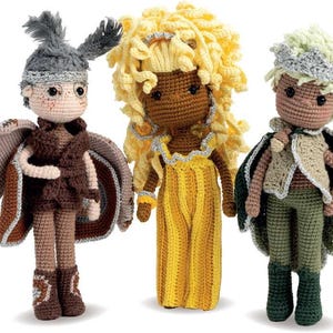May include: Three handmade crochet dolls. The doll on the left has brown wings, a gray hat, and brown clothing. The middle doll has yellow hair and a yellow dress. The doll on the right has a green cape and hat, and green pants.