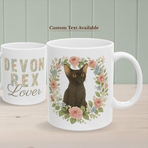 May include: White ceramic mug with a black Devon Rex cat surrounded by a floral wreath of pink and blue flowers. The mug on the left has the text "Devon Rex Lover". The text "Custom Text Available" is at the top.