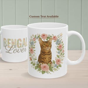 May include: White ceramic mug featuring a Bengal cat illustration surrounded by a floral wreath of pink roses and blue flowers. The mug also has the text "Bengal Lover" on the side. "Custom Text Available" is printed above the mug.
