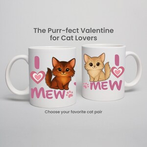 May include: Two white ceramic mugs with cat illustrations. One mug features a brown cat, the other a tan cat. Each mug has the text "I MEW" with a pink heart and paw prints. The text "The Purr-fect Valentine for Cat Lovers" is above the mugs.