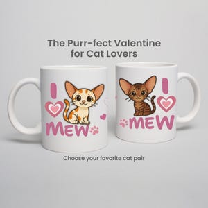 May include: Two white ceramic mugs with cat-themed designs. One mug features a cartoon orange tabby cat, the other a brown tabby. Both mugs have the text "I MEW" with a heart and paw prints. The text "The Purr-fect Valentine for Cat Lovers" is above the mugs.