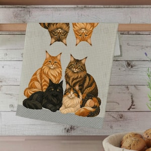 Op de afbeelding: Een lichtgroene en witgepatroneerde keukendoek met illustraties van Maine Coon katten. De handdoek toont zes katten in verschillende poses, met een mix van kleuren waaronder oranje, zwart en bruin.