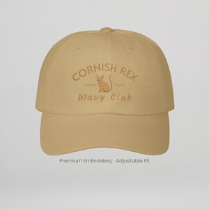 Könnte beinhalten: Beige Baseball Cap mit dem gestickten Text "Cornish Rex Wavy Club" und einer Katzenillustration. Auf der Kappe steht auch "Premium Embroidery Adjustable Fit".