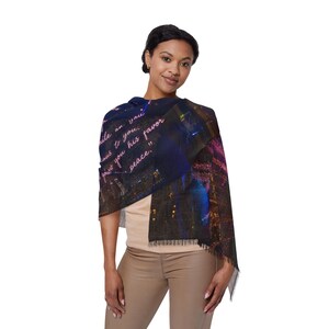 May include: A dark blue scarf with a cityscape design and fringed edges. The scarf features a quote in pink script. The scarf is draped over a person's shoulders.