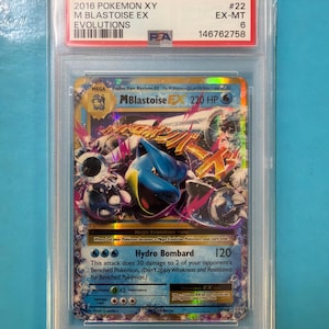 Puede incluir: Una carta Pokémon clasificada M Blastoise EX del set XY Evolutions de 2016. La carta está dentro de un soporte protector con una etiqueta roja y blanca que muestra los detalles de la carta y una calificación PSA de 6. El arte de la carta muestra un Blastoise azul.