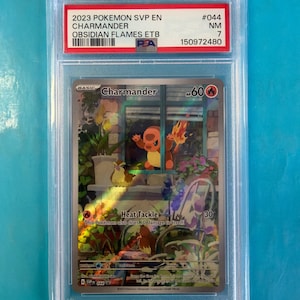 Op de afbeelding: Een beoordeelde Pokémon-ruilkaart met Charmander uit de Obsidian Flames-set. De kaart zit in een beschermende houder met een rood en wit label. De kaartkunst toont Charmander in een tuinscene met de tekst "Heat Tackle".