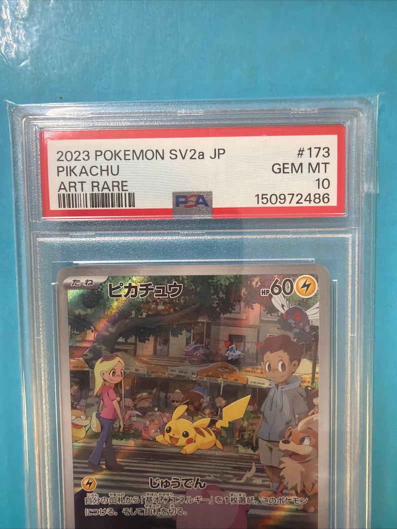 May include: A graded Pok&eacute;mon card featuring Pikachu, labeled "2023 POKEMON SV2a JP ART RARE." The card is graded GEM MT 10 by PSA. The card's artwork depicts Pikachu with other characters in a city setting.