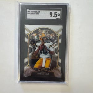 May include: A graded 2020 Panini Select #47 Jordan Love football card. The card features a player in a Packers uniform. The card is encased in a black holder with a 9.5 grade. The card is in a clear plastic sleeve.